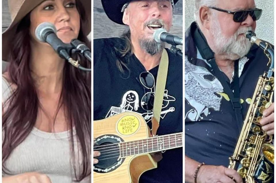 Kim with long brown hair, wearing a cowgirl hat and white tank top singing and playing keyboard, Dougie wearing a cowboy hat and black collared shirt, singing and playing guitar, their friend with white hair and beard wearing sunglasses, black and white shirt and playing saxophone