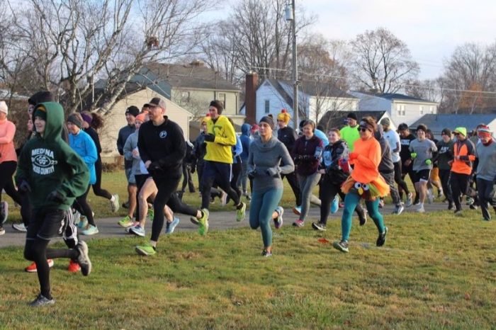 A crowd of people dressed for chilly weather running a race in the grass and on a path