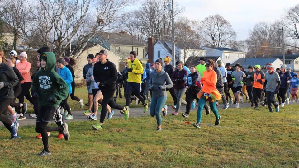 A crowd of people dressed for chilly weather running a race in the grass and on a path
