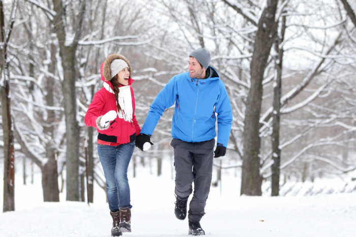 A couple walking in the woods in the snow laughing and enjoying themselves