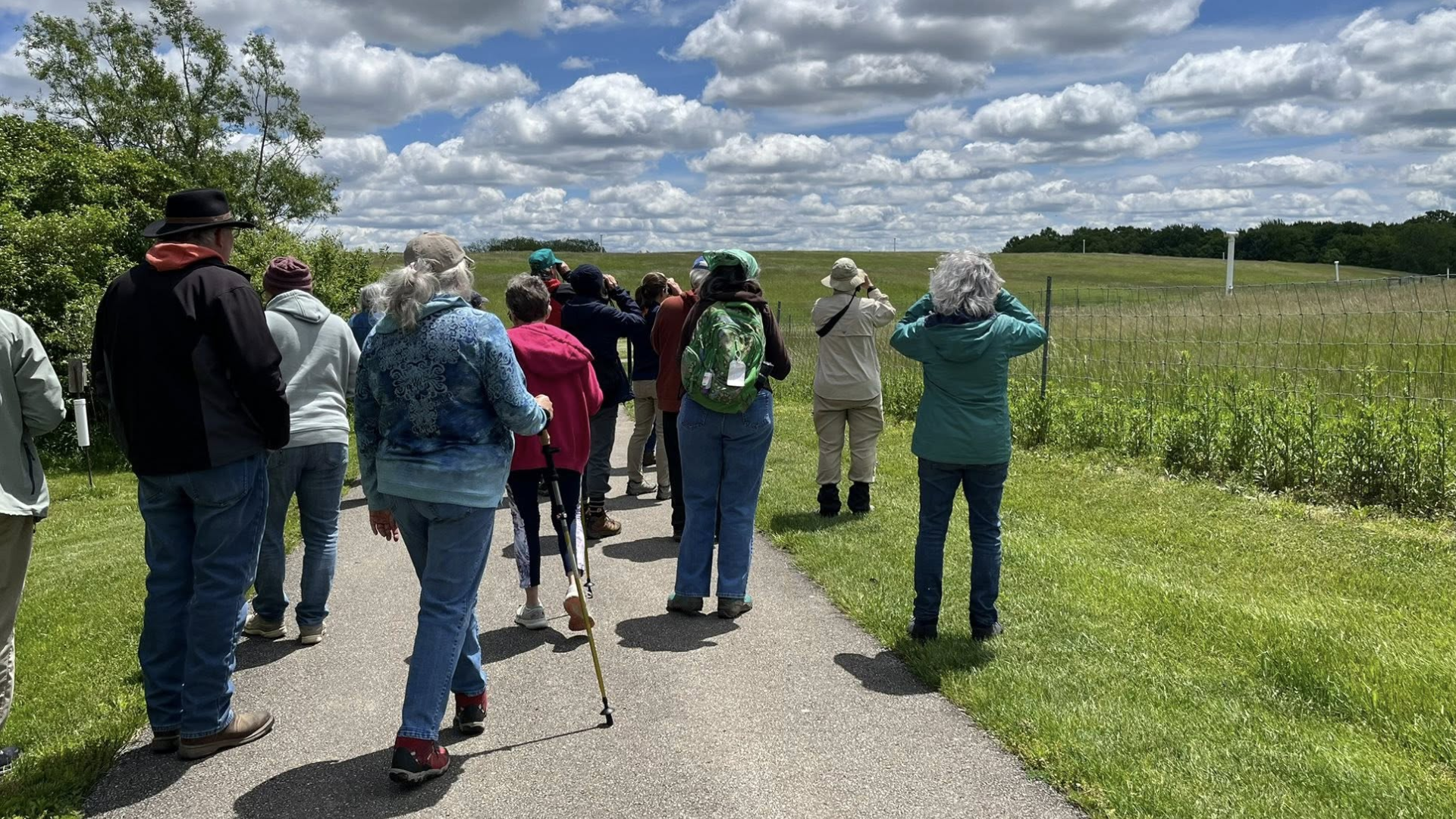 people wearing jackets and hoodies and hats on a hike on a beautiful sunny day outside with white fluffy clouds