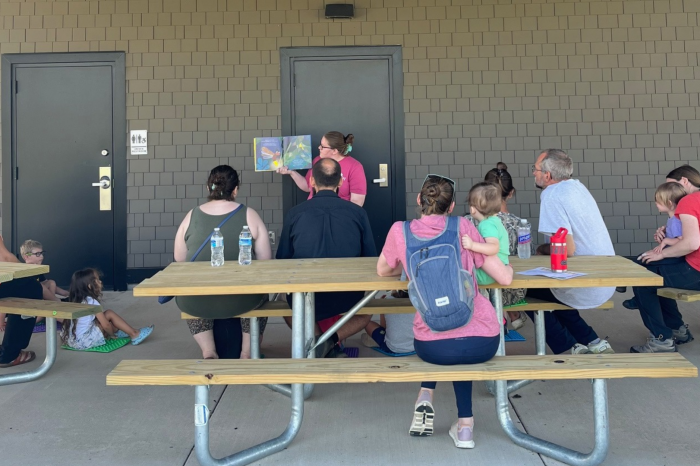 caregivers and kids gathered around someone holding up and reading a picture book before going on a short walk