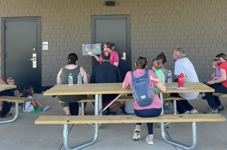 caregivers and kids gathered around someone holding up and reading a picture book before going on a short walk