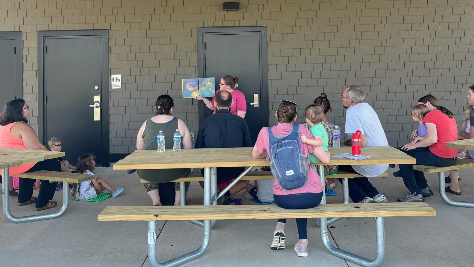 caregivers and kids gathered around someone holding up and reading a picture book before going on a short walk