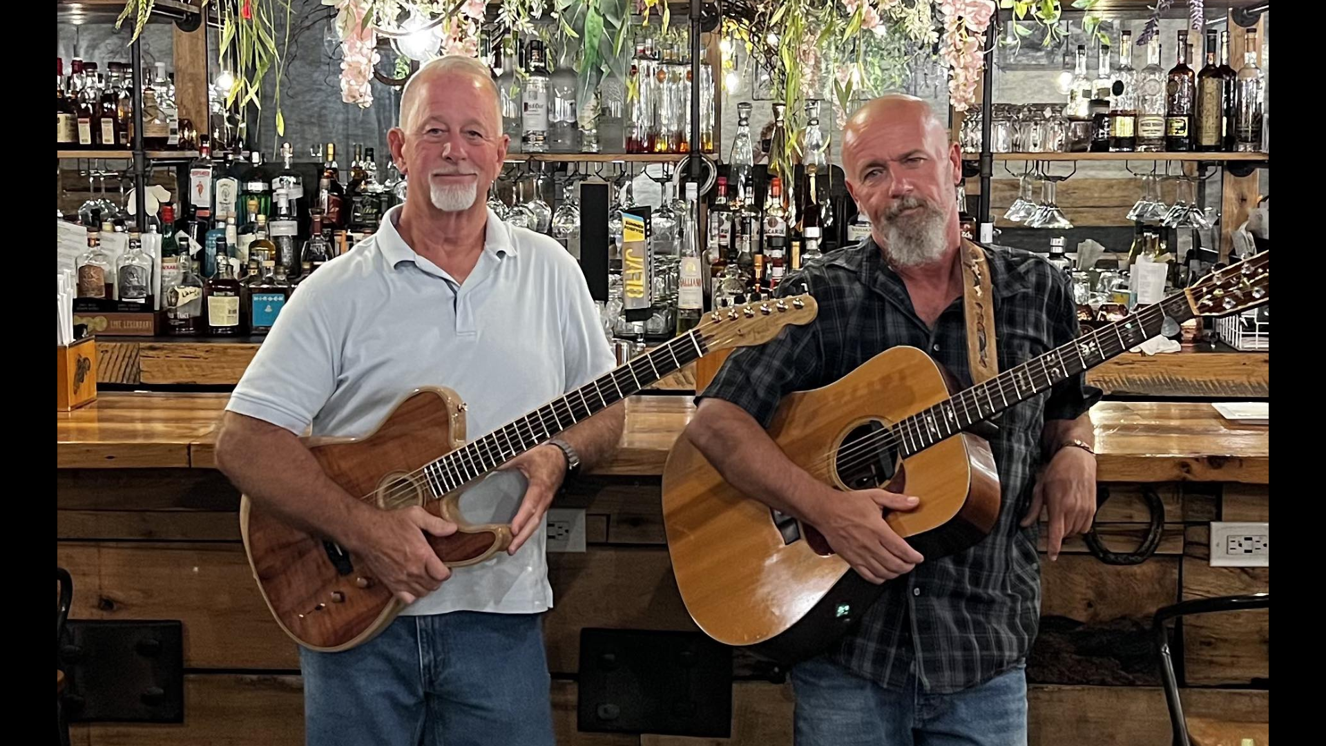 Steve and Sam leaning against a bar with their guitars