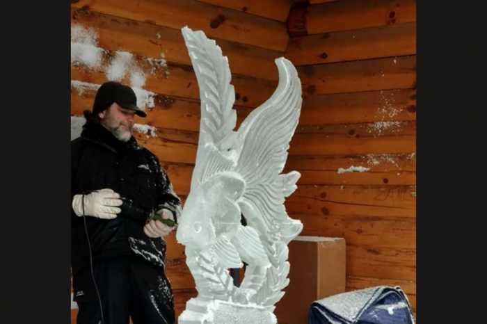 A man wearing black clothes, a black ball cap and white gloves working on creating an ice sculpture for a demo as part of the Mohican Winterfest